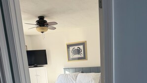A bedroom with a bed, a ceiling fan, a framed picture on the wall, and a television on a cabinet. - Coastal modern 2-bedroom condo in lovely Wells with water views (Wells)