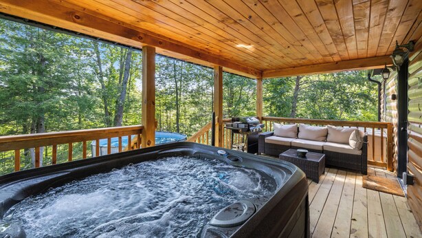Une terrasse en bois avec un jacuzzi, un coin salon extérieur et une vue sur la forêt.