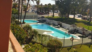 A pool area with a curved design, surrounded by palm trees and lounge chairs.