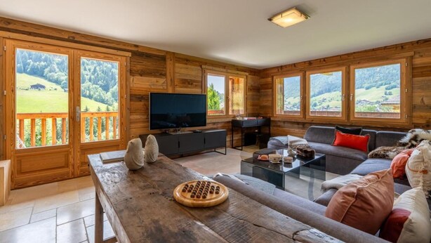 Una cabaña de madera con una televisión grande, un sofá, una mesa de centro y una mesa de madera con un juego de mesa.