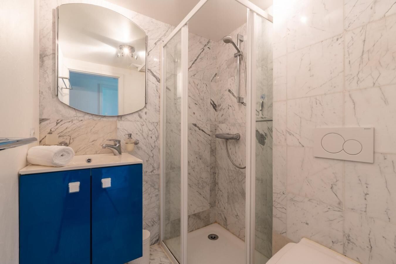 A bathroom with a marble wall, a blue cabinet, a mirror, and a shower.