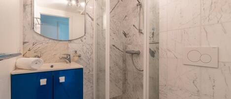 A bathroom with a marble wall, a blue cabinet, a mirror, and a shower.