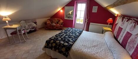 A bedroom with a bed, a chair, a table, and a window.