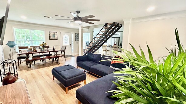 A spacious living room with a dark blue sofa, wooden flooring, a ceiling fan, and a staircase leading to an upper level. - Peaceful Mableton Retreat Near Atlanta’s Vibrance (Mableton)