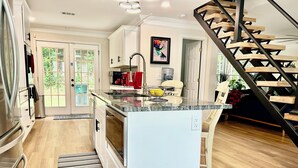 A modern kitchen with a central island, white cabinetry, and a wooden staircase. - Peaceful Mableton Retreat Near Atlanta’s Vibrance (Mableton)