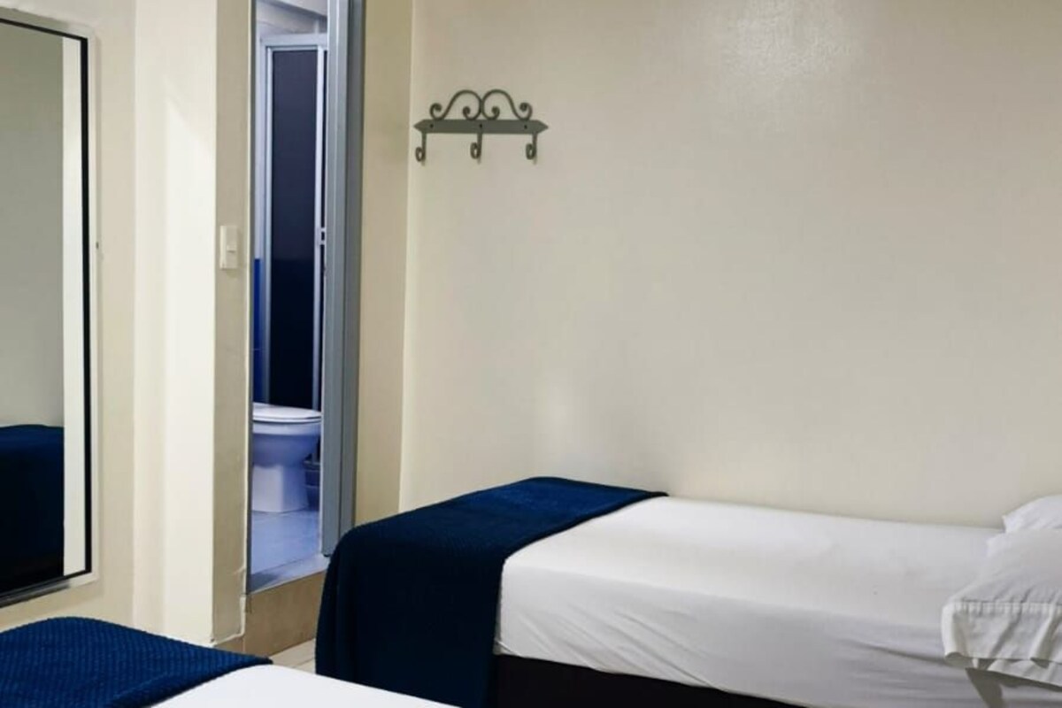 Een hotelkamer met twee bedden, een deur naar een badkamer en een klein wandlampje.