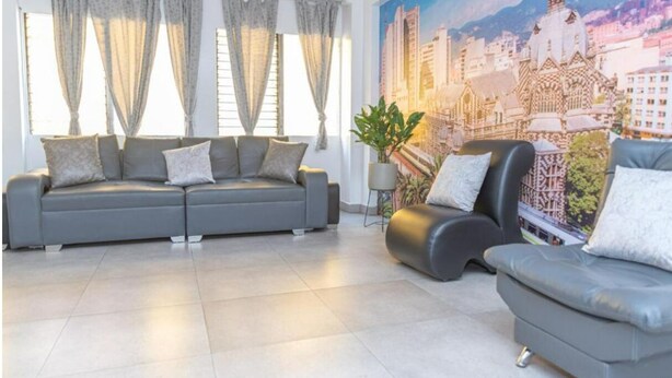 A modern living room with a grey sofa set, a black armchair, and a cityscape mural on the wall. - Hotel Alcazar Medellin (Medellín)