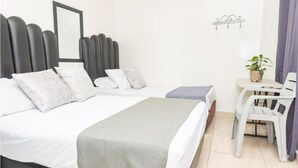 A hotel room with two beds, a small table, a chair, and a potted plant. - Hotel Alcazar Medellin (Medellín)