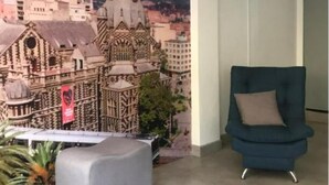 A room with a mural of a cityscape, a grey ottoman, and a blue armchair. - Hotel Alcazar Medellin (Medellín)