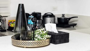 Una encimera de cocina con una bandeja decorativa que sostiene un vaso, un objeto negro y un ramo de flores blancas.