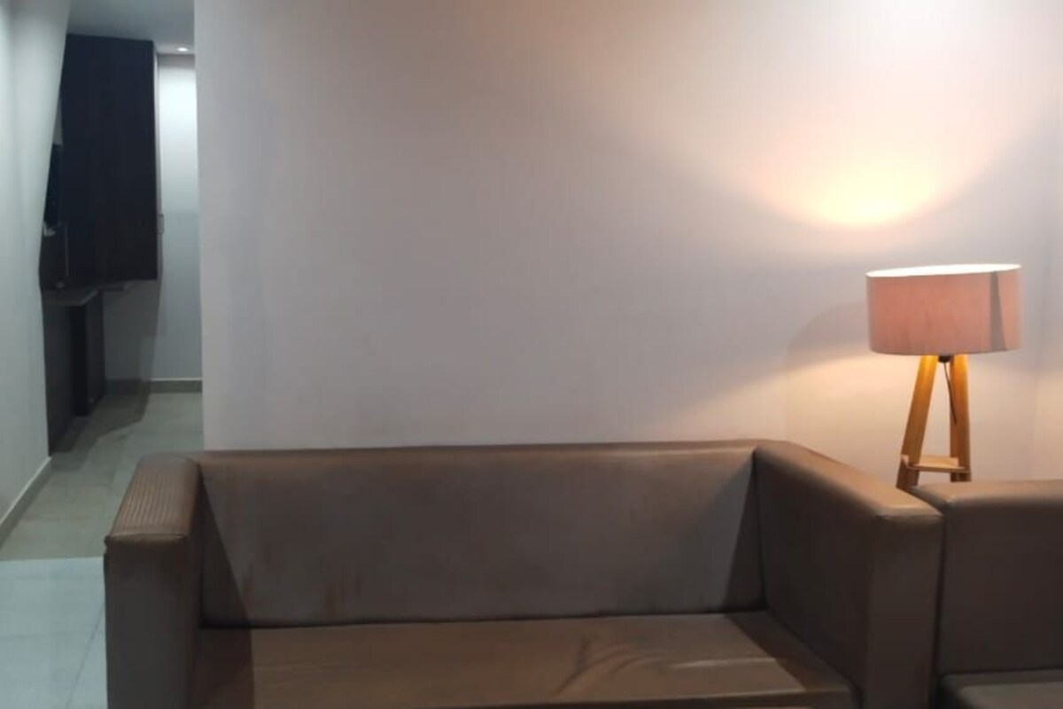 A room with a sofa, a lamp, and a hallway leading to another room.