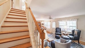 Ein geräumiges Wohnzimmer mit Holztreppe, Deckenventilator und großem Fenster für natürliches Licht.