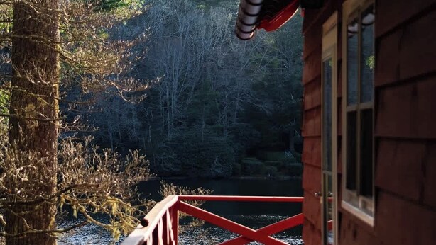 Eine Holzterrasse mit roter Geländer, mit Blick auf ein bewaldetes Gebiet.
