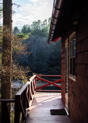 A wooden deck with a red railing overlooking a forested area.