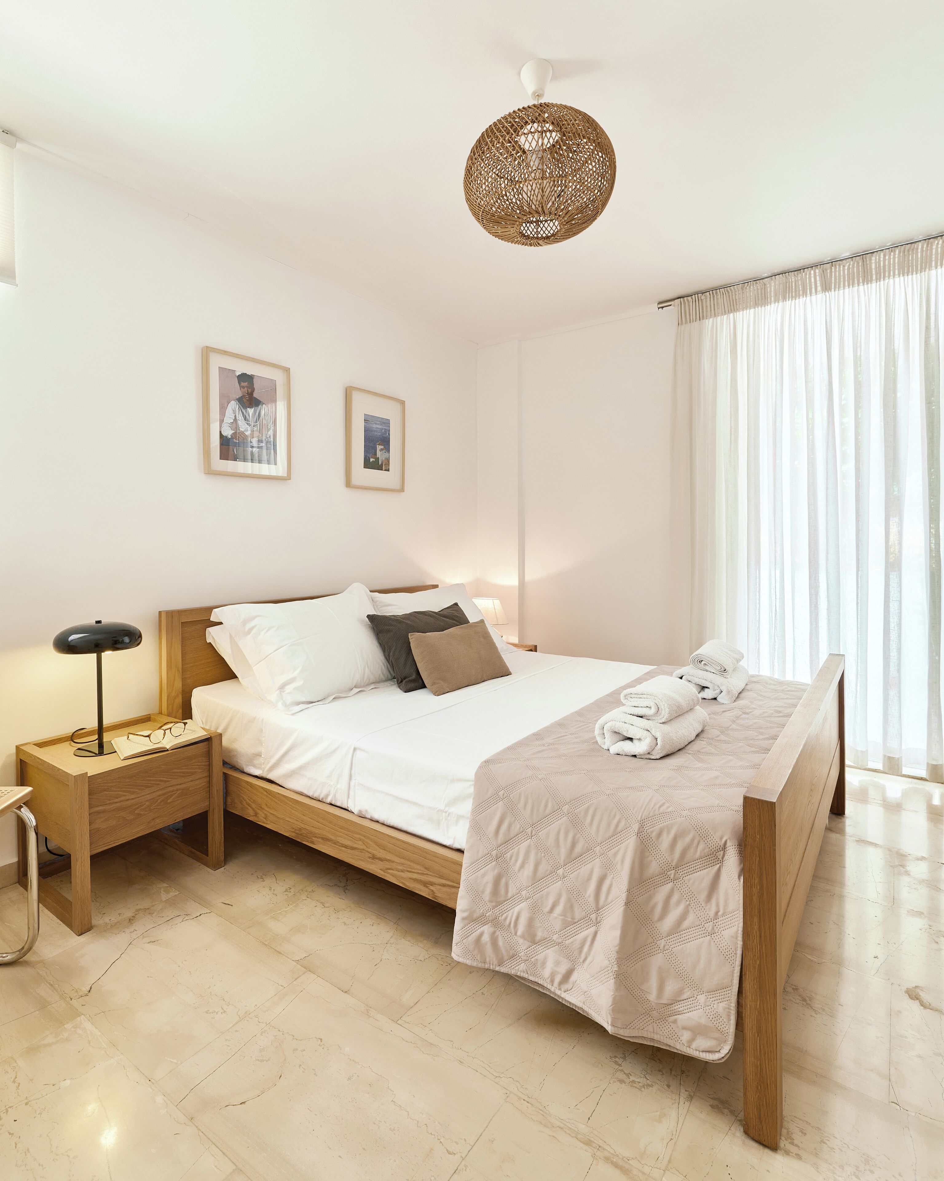 Ein ordentlich eingerichtetes Schlafzimmer mit einem hölzernen Bett, einem Nachttisch mit Lampe und zwei gerahmten Bildern an der Wand.