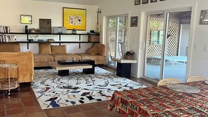 A spacious living room with a ceiling fan, a large rug, a dining table with a patterned tablecloth, and a bookshelf with various items. - Relaxing house with spacious dock tucked on Gordon River. Live the Florida dream (Naples)