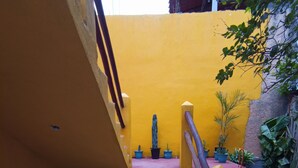 A staircase with yellow railings leading to a landing, surrounded by potted plants and a wooden bench. - Posada Antonia (Bacalar)