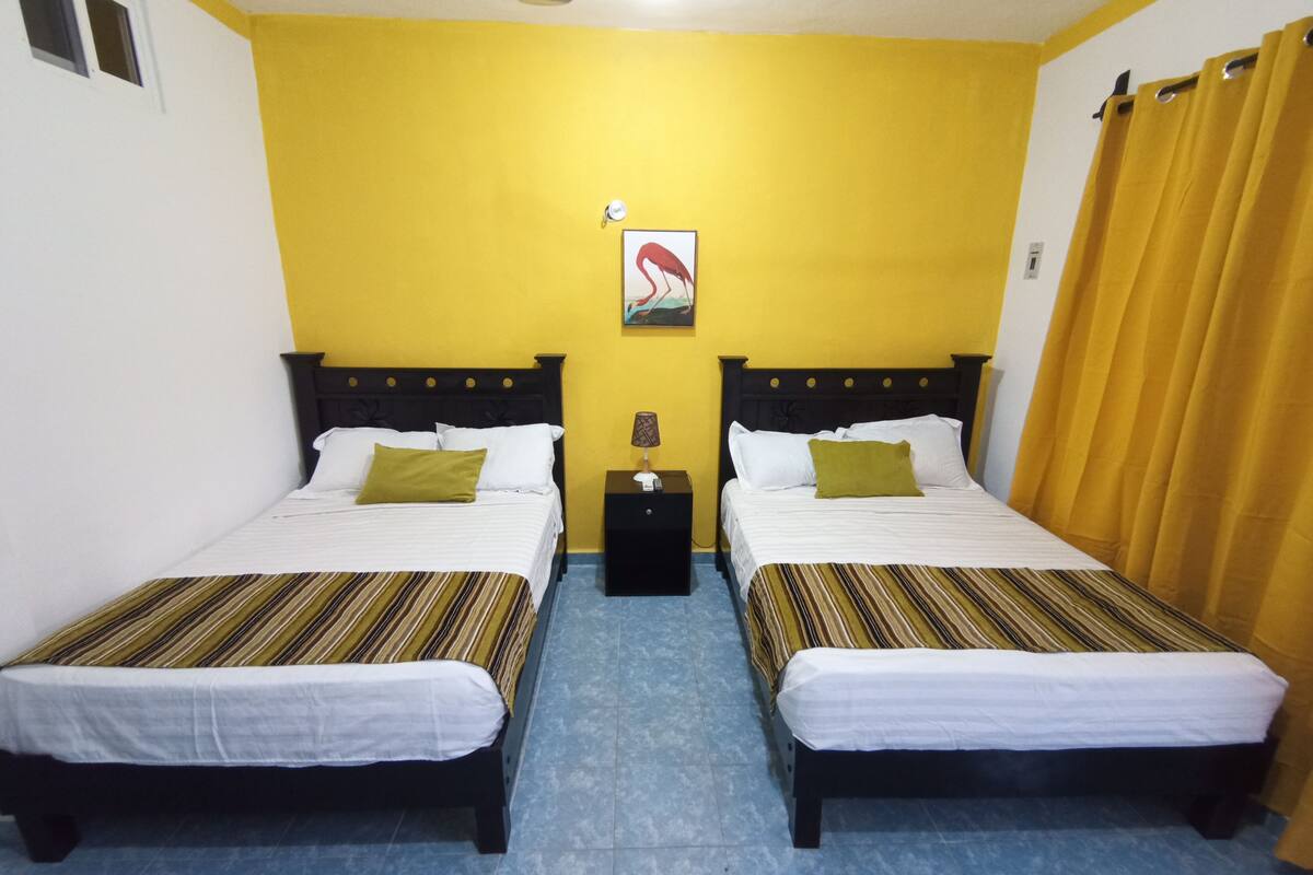 A room with two beds, each with a striped bedspread, a nightstand, a lamp, and a wall-mounted picture.