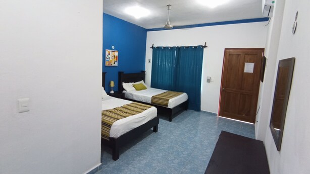 A room with two beds, a wooden door, a ceiling fan, and a wall-mounted air conditioner. - Posada Antonia (Bacalar)