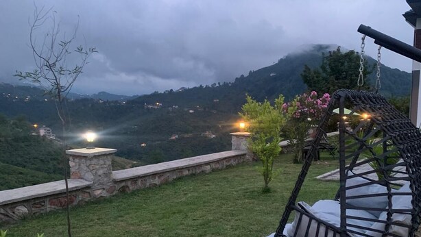 A grassy outdoor area with a stone wall, a hanging swing chair, and a stone lantern. - Çiftlikte Konaklama Villa Saklı Bahçe (ordu)