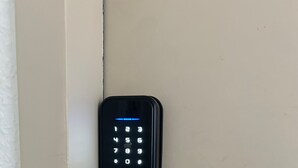 Ein schwarzes elektronisches Zahlenschloss mit Griff, angebracht an einer beigen Tür.