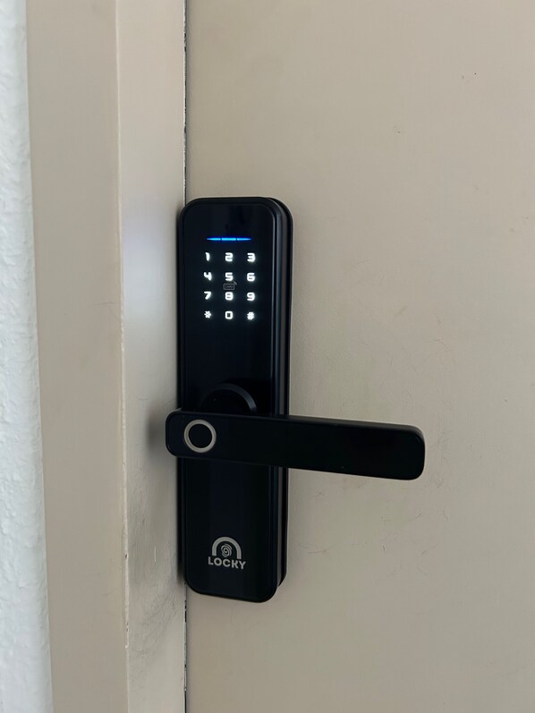 A black electronic keypad lock with a handle, mounted on a beige door.