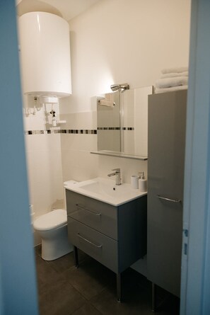 A bathroom with a toilet, sink, mirror, and cabinet. - Cozy studio in the heart of Pornic (Pornic)