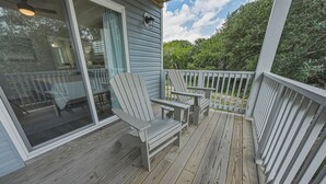 A wooden deck with Adirondack chairs, a table, and a glass door leading to a room. - HOT TUB! Four bedroom home in the 4X4, Corolla, NC. A truly unique getaway! (Corolla)