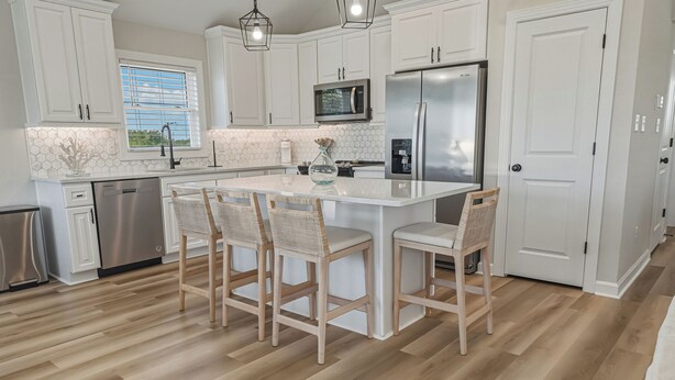 A modern kitchen with white cabinets, a stainless steel refrigerator, a microwave, and a large island with bar stools. - HOT TUB! Four bedroom home in the 4X4, Corolla, NC. A truly unique getaway! (Corolla)