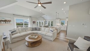 A spacious living room with a large L-shaped sectional sofa, a round wooden coffee table, and a ceiling fan. - HOT TUB! Four bedroom home in the 4X4, Corolla, NC. A truly unique getaway! (Corolla)