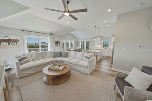 A spacious living room with a large L-shaped sectional sofa, a round wooden coffee table, and a ceiling fan.