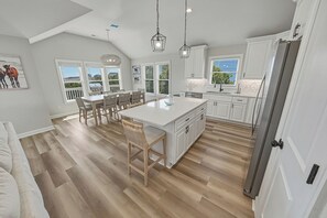 A spacious kitchen with a large island, white cabinetry, and a dining area with a view. - HOT TUB! Four bedroom home in the 4X4, Corolla, NC. A truly unique getaway! (Corolla)