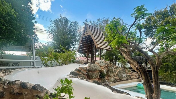 Un área de piscina con un pabellón de madera, rodeado de rocas y follaje.
