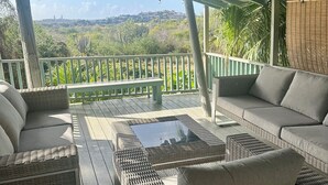 Een overdekt terras met rieten meubilair en uitzicht op een veraf gelegen landschap.