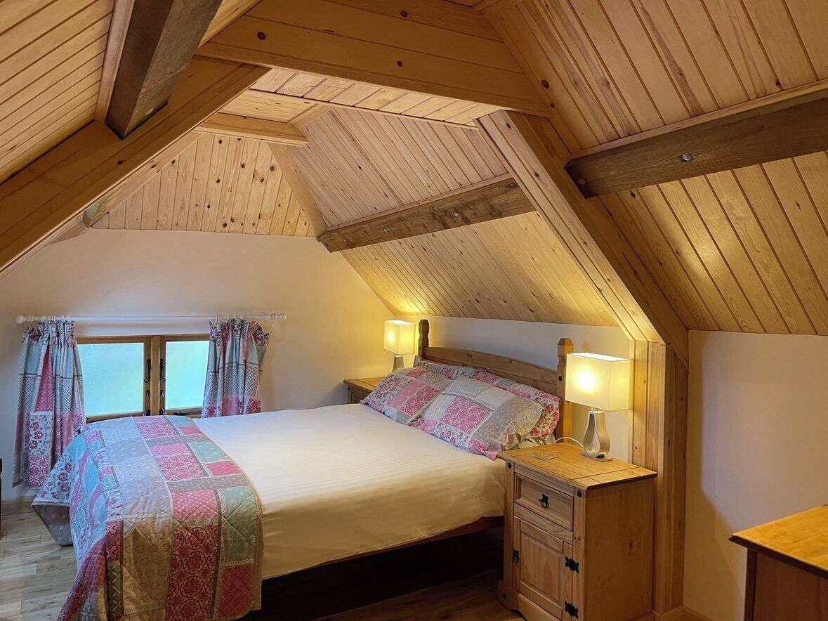 A cozy attic bedroom with a sloped ceiling, a bed with a quilt, bedside lamps, and a wooden nightstand.