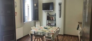 Un pequeño comedor con una mesa y sillas, un televisor montado en la pared y una estantería con libros.