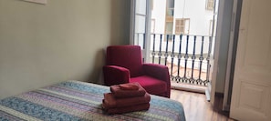 A room with a bed, a red chair, and a balcony with a railing.