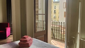 Ein Zimmer mit einem Bett, einem roten Sessel und einem Balkon mit Metallgeländer.