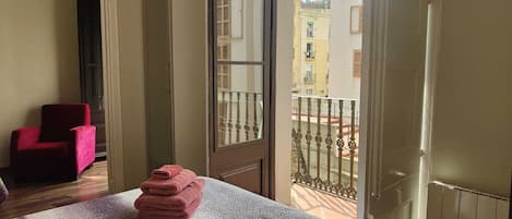 A room with a bed, a red chair, and a balcony with a metal railing.