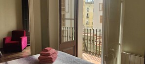 A room with a bed, a red chair, and a balcony with a metal railing. - Acomodis great location right in El Born old town 4 air conditioners 6 ppl max.! (Barcelona)