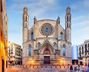 A historic church with a large circular stained glass window, a central entrance, and two bell towers.