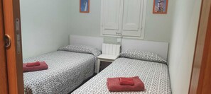 A small, simple room with two beds, each with a patterned bedspread and a red towel. There is a white radiator between the beds and a small table. - Acomodis great location right in El Born old town 4 air conditioners 6 ppl max.! (Barcelona)
