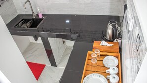 Une cuisine moderne avec un plan de travail noir, un évier et une bouilloire. On peut voir un plateau en bois avec des assiettes et des verres posés sur le plan de travail.