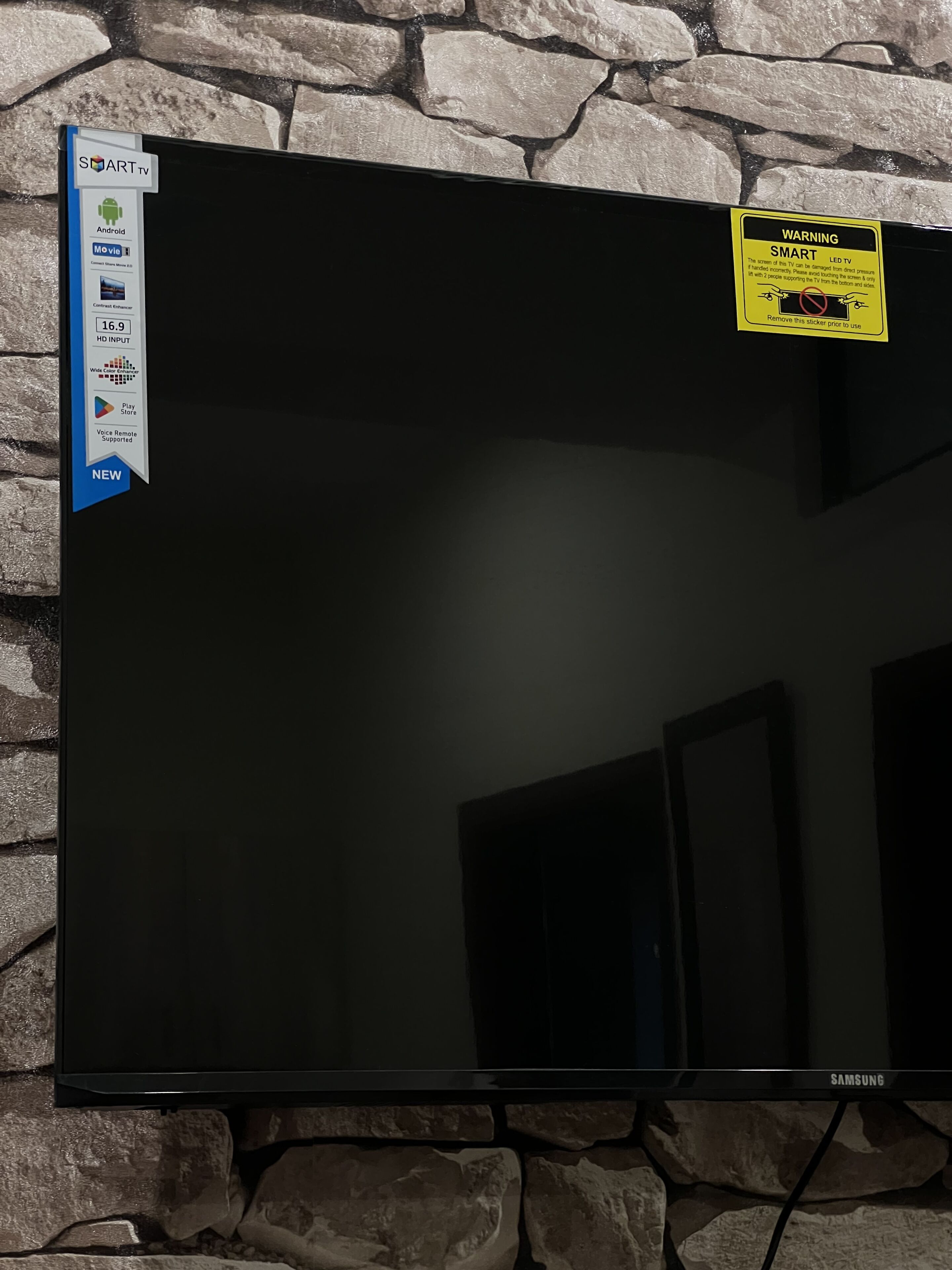 Et fladskærms-TV monteret på en stenvæg, med klistermærke der angiver at det er et Samsung Smart TV.