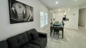 Una sala de estar moderna con un sofá gris oscuro, una zona de comedor con una mesa dispuesta para cuatro personas y una cocina al fondo.