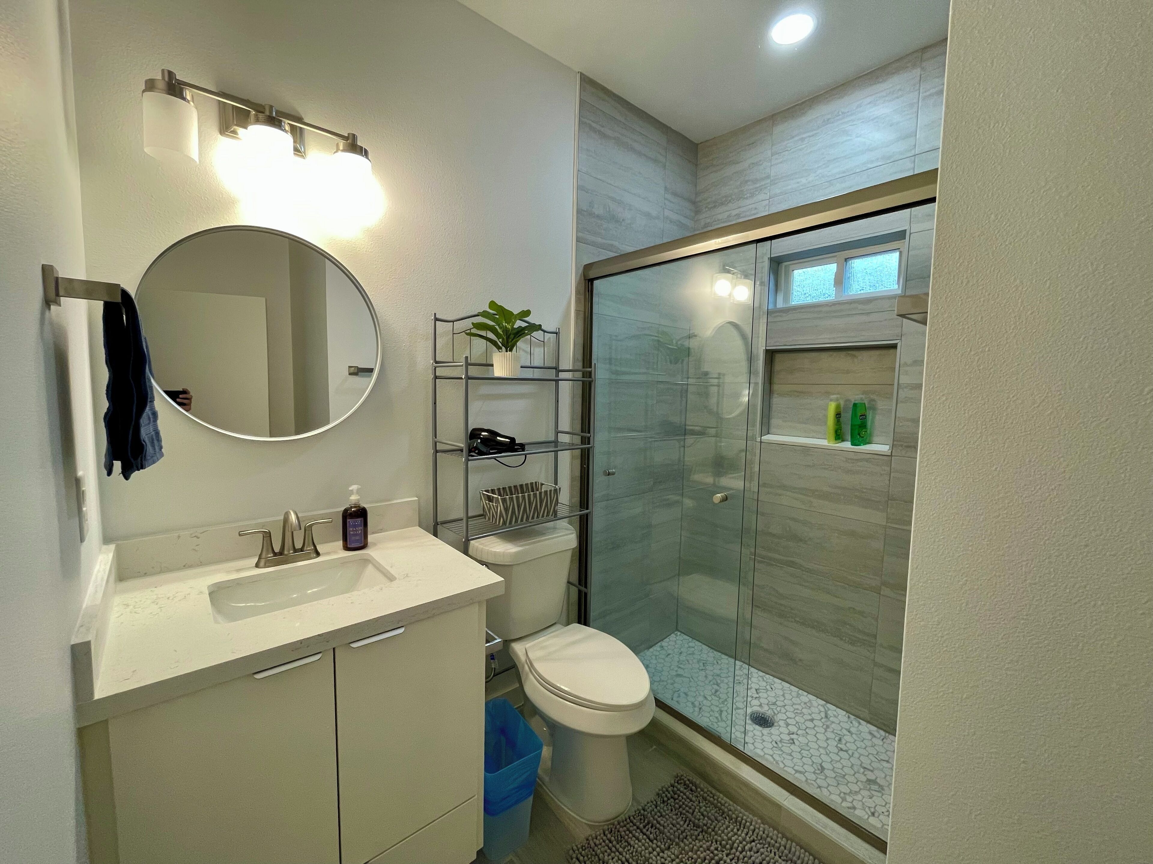 A modern bathroom with a round mirror, white sink, and a glass-enclosed shower.