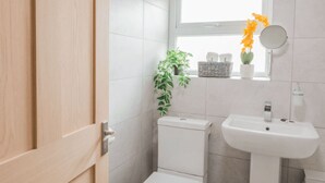 A modern bathroom with a toilet, sink, and a window with a plant. - Chic city flat with parking, near the waterfront (Stonehouse)