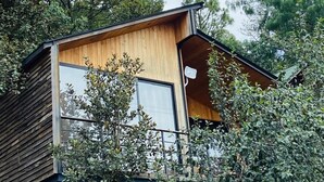 Een moderne houten blokhut met balkon, omringd door dichte begroeiing.