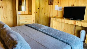 Een houten kamer met een bed, een televisie en een klein bureau.