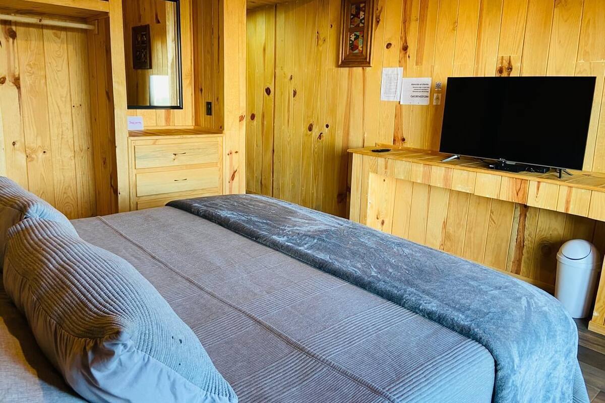 A wooden cabin room with a bed, a television, and a small desk.